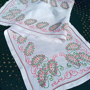 May include: White table runner with a paisley pattern embroidered in red, green, yellow, and purple thread.