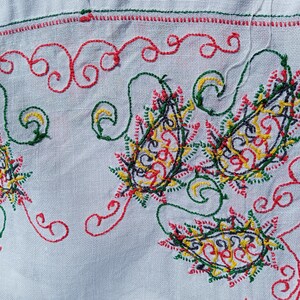 May include: White fabric with intricate embroidery in red, green, yellow, and black. The design features paisley shapes and swirls.