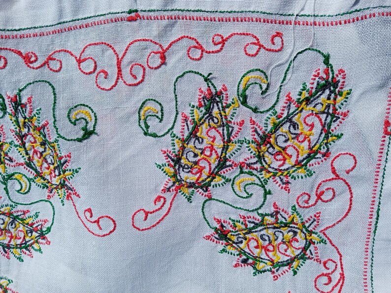 May include: White fabric with intricate embroidery in red, green, yellow, and black. The design features paisley shapes and swirls.