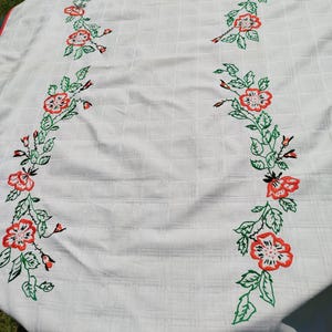 Puede incluir: Mantel blanco con un diseño floral bordado en rojo y verde. El mantel tiene un borde rojo.