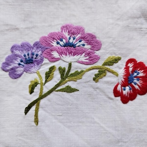 May include: Embroidered flowers in shades of pink, purple, and red on a white linen fabric. The flowers are stylised and have a vintage look.