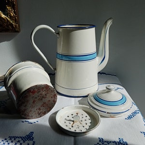 May include: White enamel coffee pot with blue stripes, a white enamel filter, and a white enamel lid with blue stripes. The coffee pot is sitting on a white tablecloth with a blue and white pattern.
