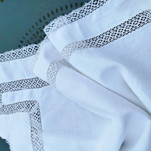 May include: White linen tablecloth with delicate lace trim. The lace is a geometric pattern with a white background.
