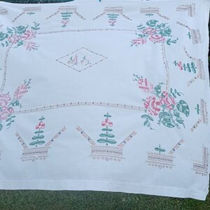 May include: White tablecloth with embroidered floral designs in pink, green, and brown. The design features repeating patterns of flowers, leaves, and baskets.