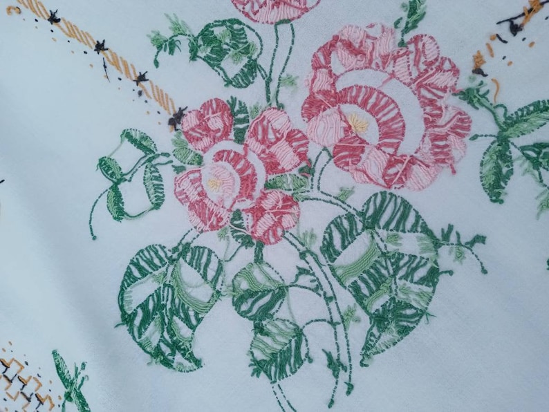 May include: White fabric with embroidered pink and green flowers. The flowers are detailed with pink and white stitching. The leaves are green with a striped pattern.