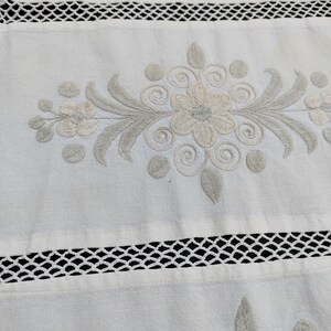 May include: White fabric with a delicate embroidered floral design in shades of gray and white. The fabric has a lace trim along the bottom edge.