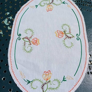 May include: White oval table runner with a scalloped edge and embroidered with orange, yellow, and green flowers.