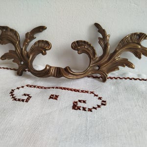 Op de afbeelding: Een decoratieve messing deurgreep met een bloemmotief. De greep is versierd en heeft een vintage stijl.