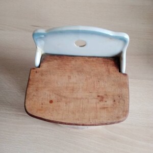 May include: A white ceramic wall-mounted spice rack with a wooden lid. The rack has a round hole in the top and a blue and white trim.