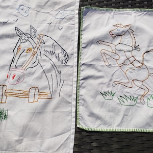 Peut inclure: Deux pièces de tissu rectangulaires blanches avec des broderies faites à la main. La pièce de gauche montre une tête de cheval derrière une clôture avec des nuages et des oiseaux. La pièce de droite représente un cheval cabré avec une bordure verte.