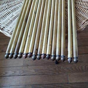 May include: A collection of antique brass curtain rods, each with a decorative finial. The rods are arranged in a fan shape, resting on a wooden surface. The finials have a variety of shapes and colours, adding visual interest to the display.