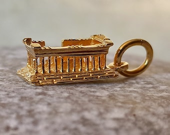 Puede incluir: Un charm de oro en forma de templo griego con un bucle para sujetarlo a un collar o pulsera.