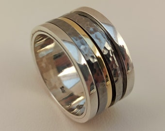 Puede incluir: Un anillo giratorio de plata y negro con una fina banda dorada. El anillo tiene una textura martillada.