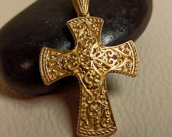 May include: A gold-toned cross pendant with intricate filigree detailing. The cross has a rounded, ornate design and a loop at the top for attaching to a chain.