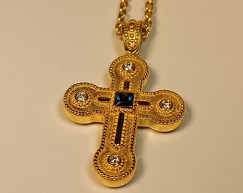 May include: A gold cross pendant with a blue sapphire and clear diamonds. The cross is detailed with a textured border and a chain.