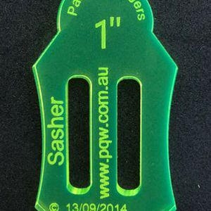 May include: A green plastic template for a 1-inch sash buckle. The template is labeled "Pauline Rogers" and "Sasher" with the website "www.pqw.com.au" and the date "13/09/2014".