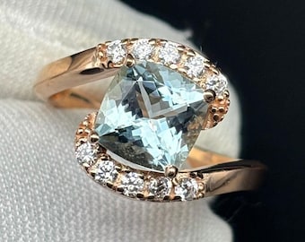 May include: A rose gold ring with a square-shaped aquamarine gemstone surrounded by a halo of smaller diamonds.