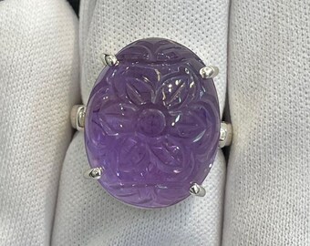 May include: A silver ring with a carved amethyst gemstone. The gemstone is a deep purple color and has a floral design.