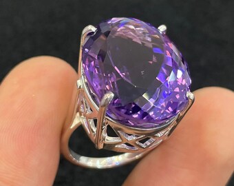 May include: A silver ring with a large, oval-shaped amethyst gemstone. The ring has a delicate, openwork design.