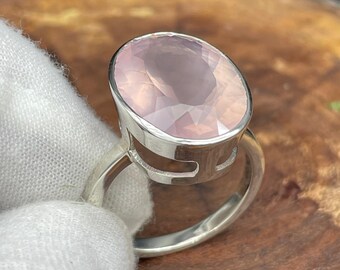 Puede incluir: Un anillo de plata con una gran piedra de cuarzo rosa ovalada de color rosa. El anillo tiene un diseño abierto único con una banda de plata.