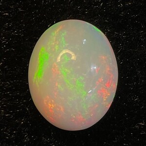 May include: A white oval opal gemstone with green, red, and orange flashes of color.