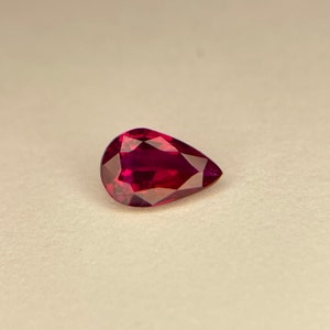 May include: A pear-shaped ruby gemstone with a deep red color.