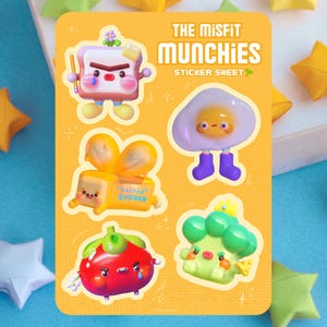 May include: A sticker sheet titled "THE MiSFIT MUNCHIES" featuring cartoon food characters. The sheet includes a slice of toast, an egg, a wrapped butter stick, a red pepper, and a broccoli floret, all with expressive faces and limbs.