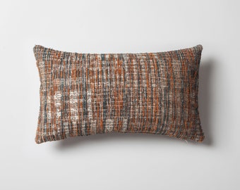 May include: A rectangular throw pillow with a woven fabric cover. The fabric is a mix of orange, gray, and white threads, creating a striped pattern.