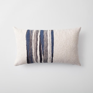 May include: Rectangular cushion with a textured off-white cover. A vertical stripe design in shades of blue, grey, and black runs down the centre. The cushion is designed for home decor and adds a touch of modern style.