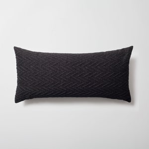 May include: A black, rectangular, textured lumbar pillow with a herringbone pattern.