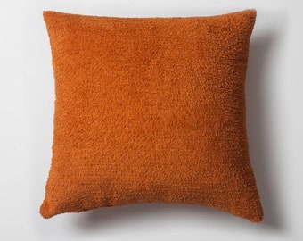 Puede incluir: Una almohada suave y mullida de color naranja quemado. La almohada está hecha de una tela suave y texturizada.