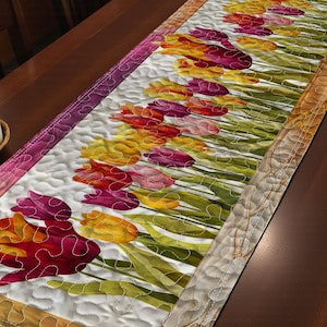 May include: A quilted table runner featuring a vibrant tulip design. The runner showcases a row of colorful tulips in shades of red, yellow, and pink against a white background. The edges are bordered with a decorative pattern.