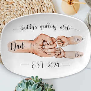 May include: White oval serving platter with the text "daddy's grilling plate" and "EST. 2024" in black. A watercolor illustration of a father's hand holding the hands of two children with the names "Dad", "Kiana", and "Rose" written next to each hand.