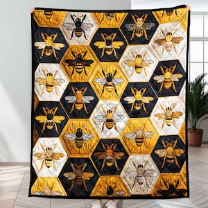 May include: A large quilt featuring a repeating pattern of bees within honeycomb-shaped cells. The quilt's design incorporates black, white, and gold colors. The bees are detailed with embroidered wings and bodies. The quilt is held up by a person.