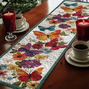 May include: A white quilted table runner with a green border, featuring colorful butterflies and flowers. The butterflies are in shades of orange, red, purple, and teal. The runner is placed on a dark wooden table, with two lit candles and teacups.