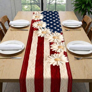May include: A patriotic table runner featuring the American flag design with white daisies. The runner has red and white stripes with a blue field of white stars. The daisies are white with yellow centers.
