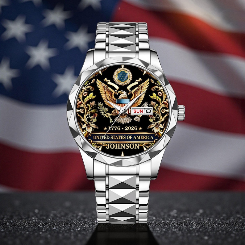 May include: A silver wristwatch with a black face featuring a golden eagle emblem, floral accents, and the text "UNITED STATES OF AMERICA." The watch also displays the date and the name "JOHNSON."