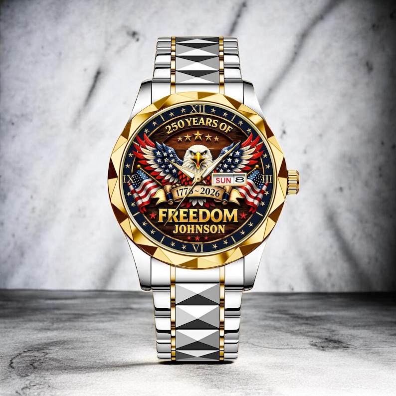 Puede incluir: Reloj de pulsera plateado y dorado con dise&ntilde;o patri&oacute;tico. La esfera del reloj presenta un &aacute;guila, banderas americanas y el texto "250 YEARS OF FREEDOM" con los a&ntilde;os 1776-2026. La correa del reloj es plateada con detalles dorados.