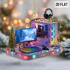 May include: A computer-themed Christmas ornament featuring a desktop computer, monitor, keyboard, and mouse. The monitor displays a winter scene. The ornament is decorated with colorful lights and the name "JAMES".