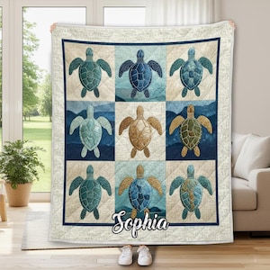 May include: A quilted blanket featuring a repeating pattern of sea turtles in shades of blue, green, and brown. The turtles are set against a backdrop of ocean-themed squares. The name "Sophia" is printed in cursive at the bottom.