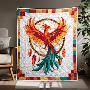 May include: A quilted blanket featuring a vibrant phoenix design. The bird is depicted with red, orange, and teal feathers, set against a white background. A dreamcatcher is behind the phoenix. The border has a patchwork design with squares of various colors.
