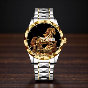 May include: A gold and silver wristwatch with a detailed gold horse design on a black face. The watch has a gold bezel and a silver band. The word "JAMES" is displayed on the watch face.