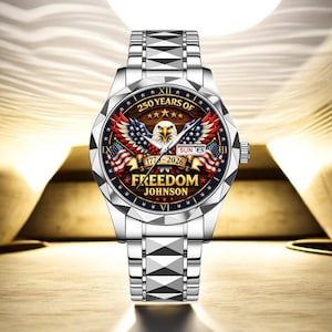 Puede incluir: Un reloj de pulsera plateado con un dise&ntilde;o patri&oacute;tico. La esfera del reloj presenta un &aacute;guila, banderas americanas y el texto "250 YEARS OF FREEDOM JOHNSON 1776-2026". El reloj tiene una correa plateada y una pantalla de fecha.
