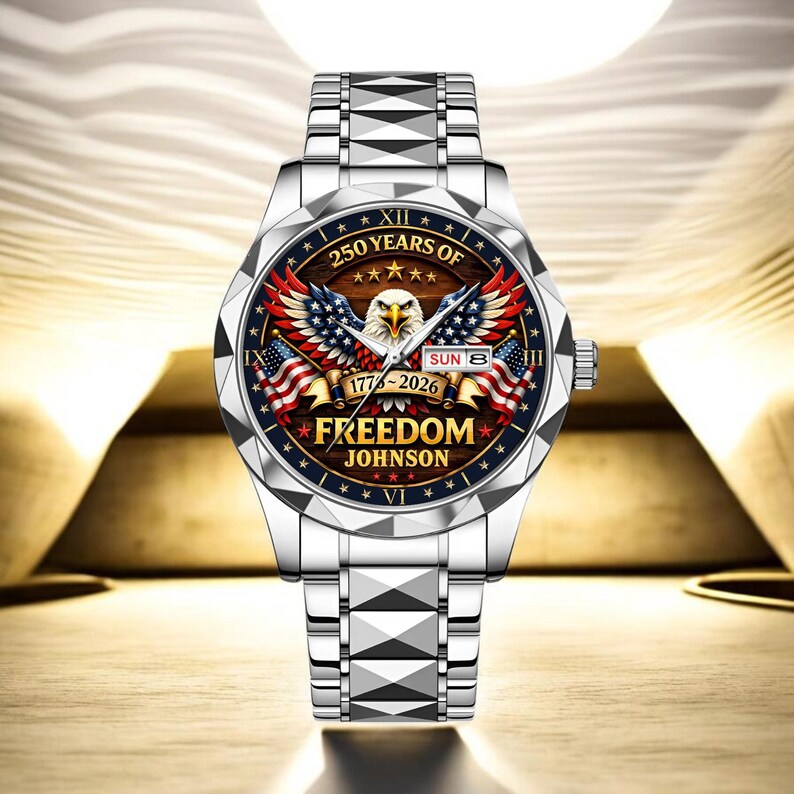 Puede incluir: Un reloj de pulsera plateado con un dise&ntilde;o patri&oacute;tico. La esfera del reloj presenta un &aacute;guila, banderas americanas y el texto "250 YEARS OF FREEDOM JOHNSON 1776-2026". El reloj tiene una correa plateada y una pantalla de fecha.
