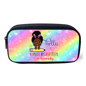 Peut inclure: Une trousse &agrave; crayons noire avec un fond arc-en-ciel et une fille de dessin anim&eacute; assise sur un crayon. Le texte "hello kindergarten I'm Kennedy" est imprim&eacute; sur la trousse.