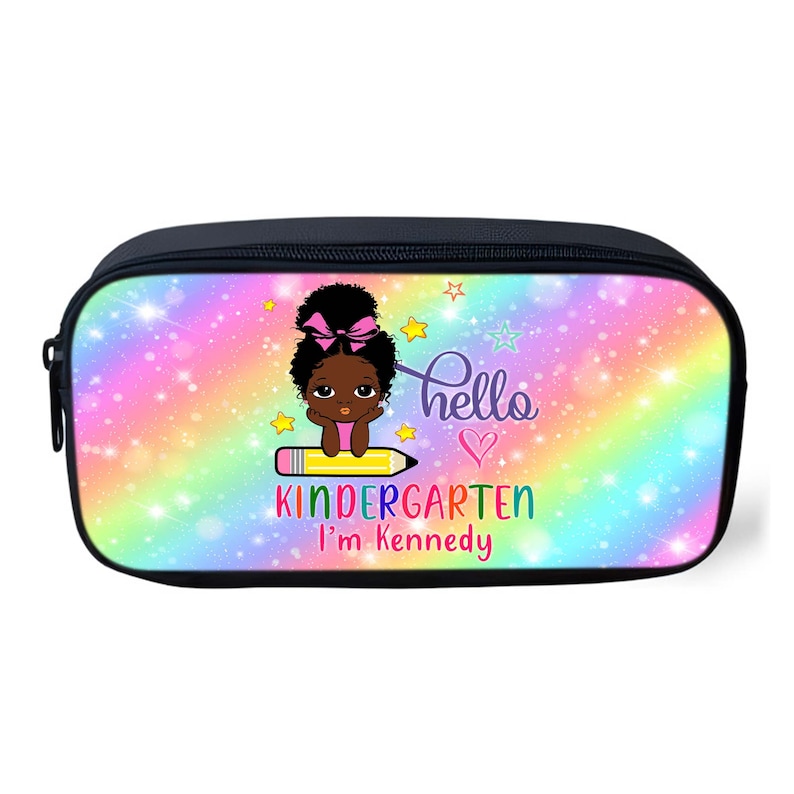 Peut inclure: Une trousse &agrave; crayons noire avec un fond arc-en-ciel et une fille de dessin anim&eacute; assise sur un crayon. Le texte "hello kindergarten I'm Kennedy" est imprim&eacute; sur la trousse.