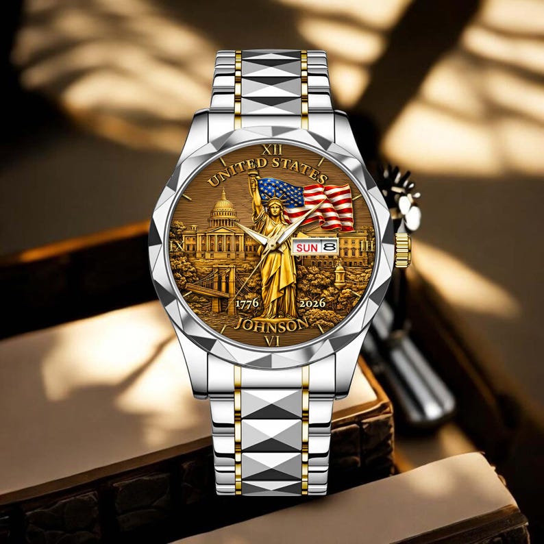 Peut inclure: Montre-bracelet argent et or avec un cadran marron repr&eacute;sentant la Statue de la Libert&eacute;, le drapeau am&eacute;ricain et le texte "UNITED STATES". Le bracelet est argent&eacute; avec des d&eacute;tails dor&eacute;s. La date est affich&eacute;e sur le cadran.