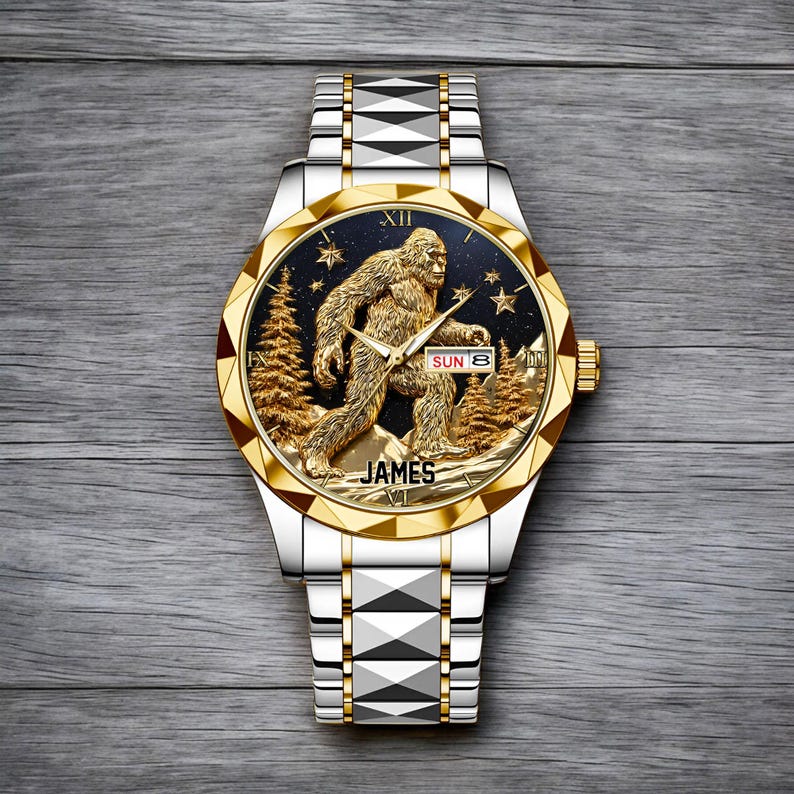 May include: A silver and gold wristwatch with a detailed Bigfoot design on the face. The watch features a gold bezel, a black dial with a Bigfoot figure, trees, and stars. The watch band is silver with geometric accents. The name "JAMES" is printed on the watch face.