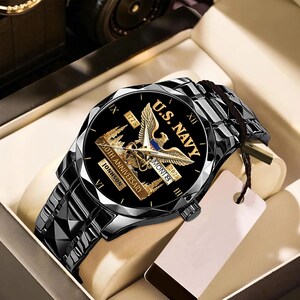 May include: A black wristwatch with a black band. The watch face features the text "U.S. NAVY" and "250th Anniversary" with an eagle emblem. The watch is presented in a gift box.