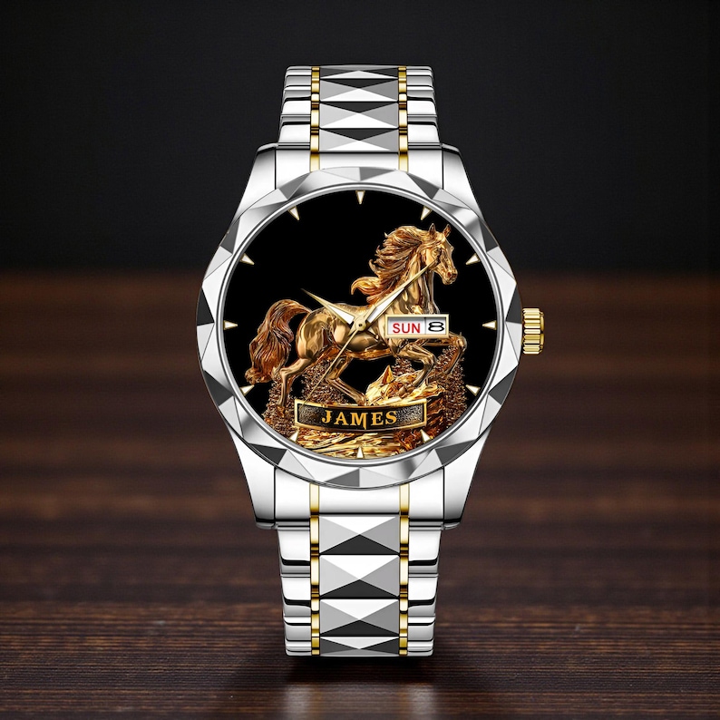 May include: Silver and gold-toned wristwatch with a black face featuring a detailed golden horse sculpture. The watch has a silver band with gold accents and the name "JAMES" is displayed on the face.